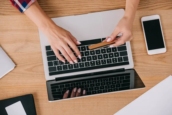 Partial view of woman with credit card making purchase online at wooden tabletop — Stock Photo