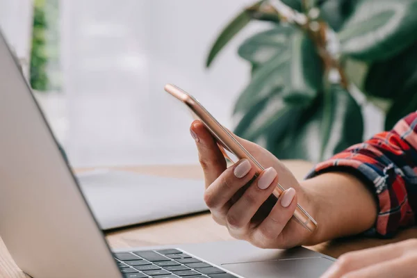 Cropped shot of businesswoman with smartphone at workplace with laptop — Stock Photo