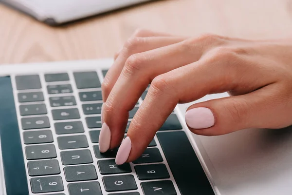 Partial view of woman typing on laptop at wooden tabletop — Stock Photo