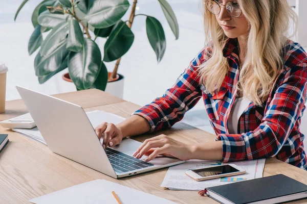 Mujer de negocios enfocada utilizando el ordenador portátil en el lugar de trabajo con papeles — Stock Photo