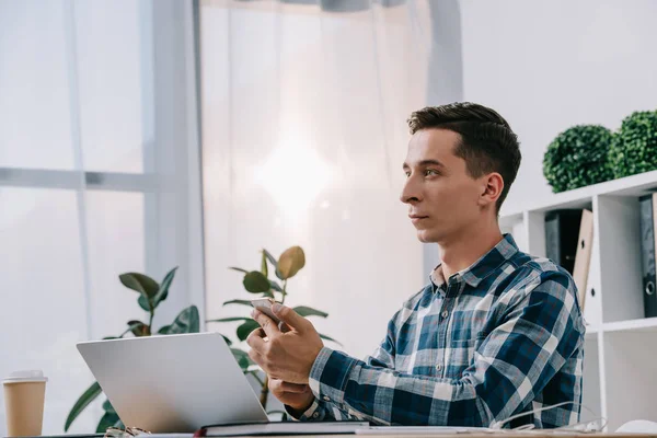 Visão lateral do empresário com smartphone sentado no local de trabalho com laptop no escritório — Fotografia de Stock