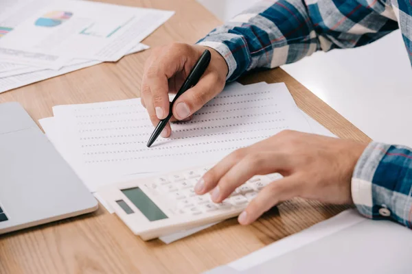 Vista parcial del hombre de negocios haciendo cálculos en el lugar de trabajo con documentos y computadora portátil - foto de stock