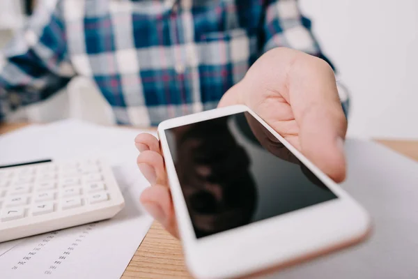 Cropped shot of businessman showing smartphone with blank screen at workplace with papers and calculator — Stock Photo