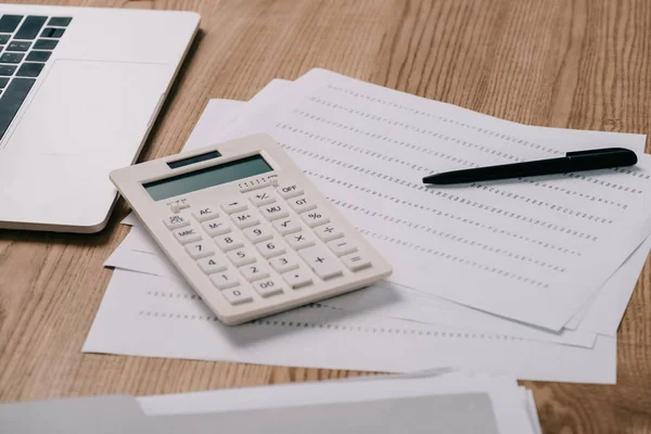 Close up view of laptop, calculator and papers on wooden tabletop — Stock Photo