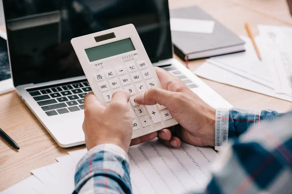 Обрезанный снимок бизнесмена с калькулятором, работающим на рабочем месте с документами и ноутбуком — стоковое фото