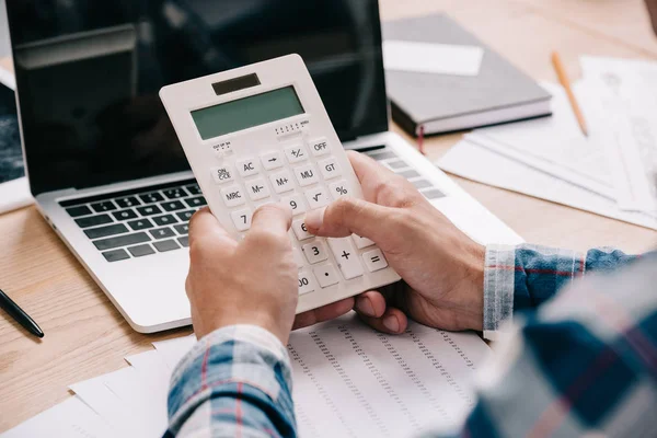 Tiro cortado de homem de negócios com calculadora trabalhando no local de trabalho com documentos e laptop — Fotografia de Stock