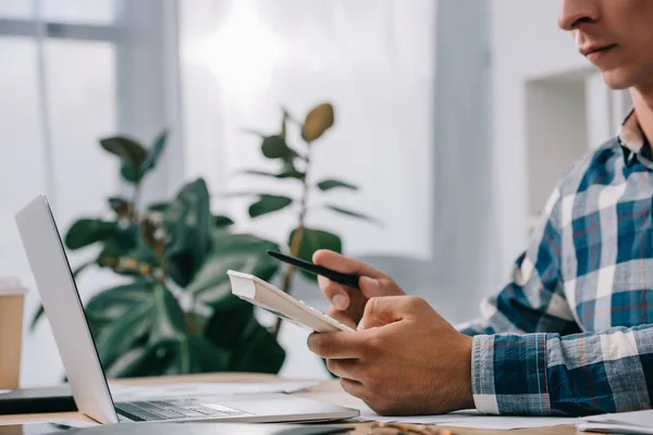 Schnappschuss eines Geschäftsmannes mit Taschenrechner, der am Arbeitsplatz mit Dokumenten und Laptop arbeitet — Stockfoto