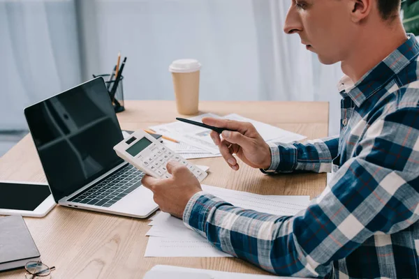 Vista parcial del hombre de negocios con calculadora trabajando en el lugar de trabajo con documentos y computadora portátil - foto de stock