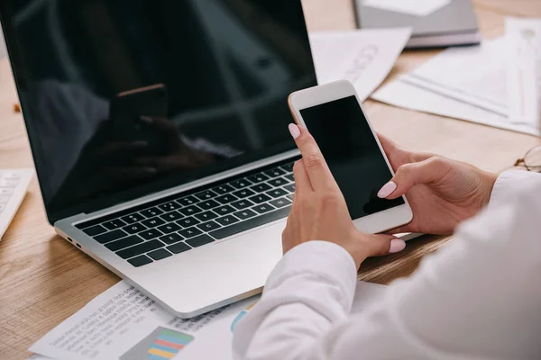 Cropped shot of businesswoman using smartphone at workpalce with laptop — Stock Photo