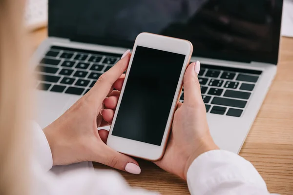 Cropped shot of businesswoman holding smartphone at workpalce with laptop — Stock Photo