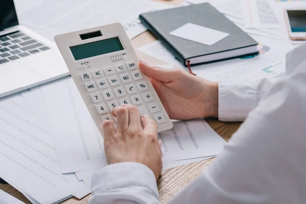 Tiro cortado de empresária fazendo cálculos sobre calculadora no local de trabalho com documentos — Fotografia de Stock