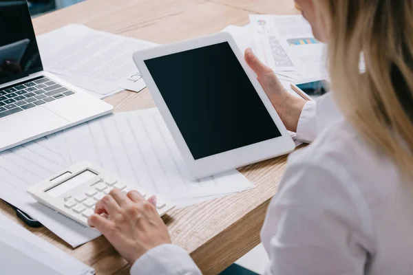 Partial view of businesswoman with tablet making calculations at workplace with papers — Stock Photo