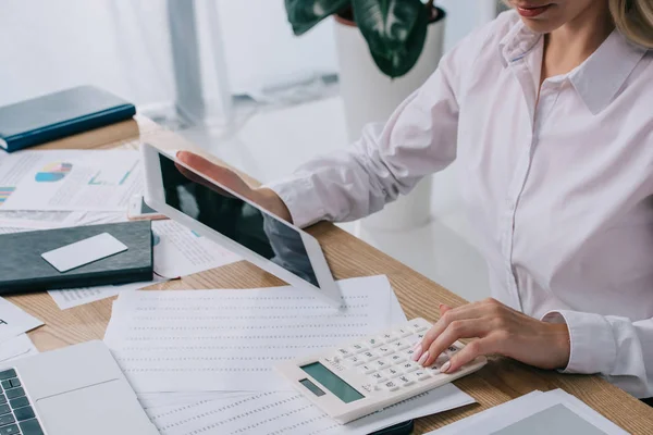 Partial view of businesswoman with tablet making calculations at workplace with papers — Stock Photo