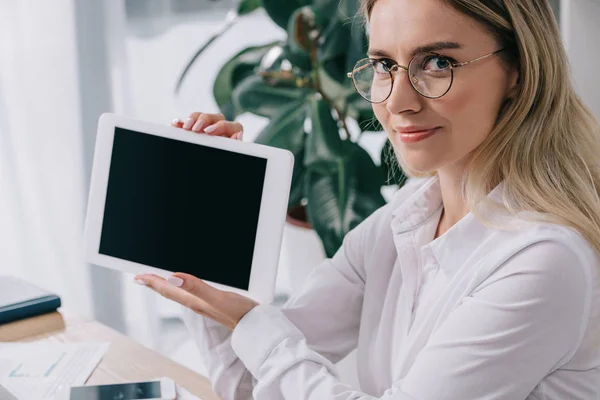 Mujer de negocios sonriente mostrando tableta con pantalla en blanco en el lugar de trabajo en la oficina - foto de stock