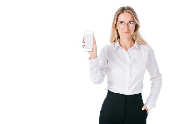 Портрет улыбающейся деловой женщины в очках, показывающий смартфон с чистым экраном, изолированным на белом — стоковое фото