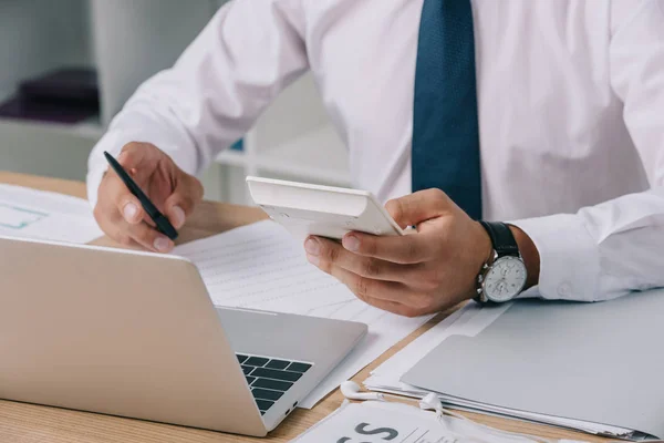 Schnappschuss eines Geschäftsmannes, der am Arbeitsplatz mit Papieren und Laptop Berechnungen anstellt — Stockfoto