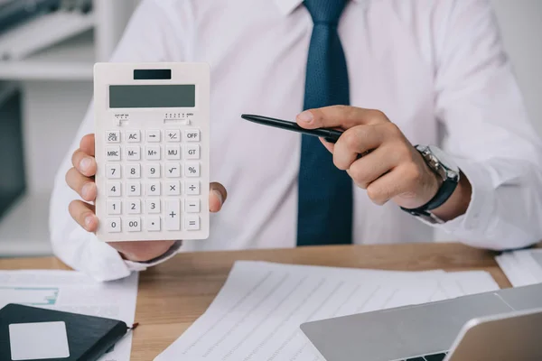 Частковий погляд бізнесмена, який вказує на калькулятор під рукою на робочому місці, концепція бухгалтерського обліку — стокове фото