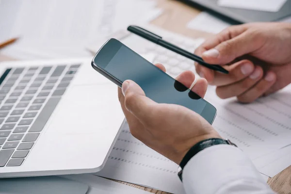 Partial view of businessman using smartphone with blank screen at workplace with papers — Stock Photo