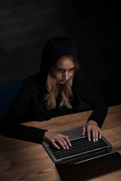 Mujer con capucha negra usando laptop, concepto de seguridad cibernética - foto de stock