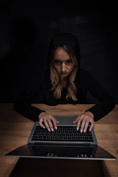 Mujer con capucha negra usando laptop, concepto de seguridad cibernética - foto de stock