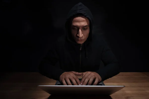 Portrait of concentrated hacker in black hoodie using laptop, cuber security concept — Stock Photo