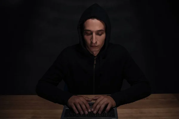 Portrait of hacker in black hoodie using laptop, cuber security concept — Stock Photo