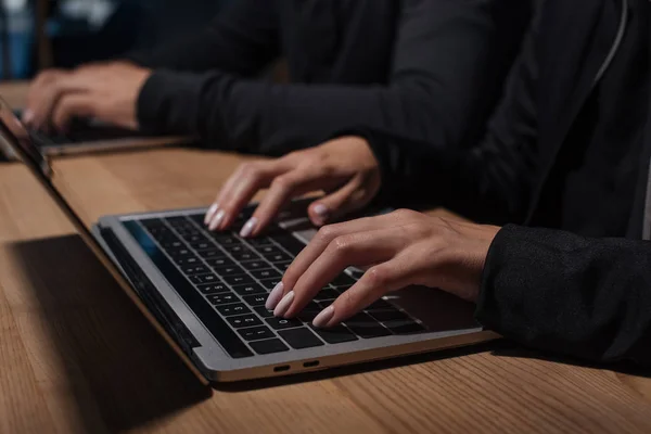 Recortado tiro de los piratas informáticos que utilizan computadoras portátiles en la mesa de madera, concepto de seguridad cibernética - foto de stock