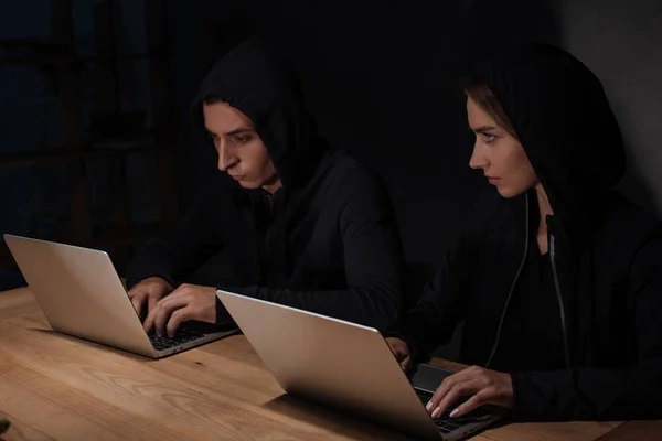 Hackers in black hoodies using laptops at wooden tabletop, cyber security concept — Stock Photo