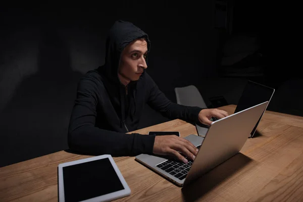 Hacker in black hoodie using laptops in dark room, cyber security concept — Stock Photo