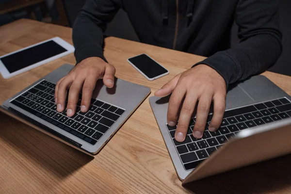 Visão parcial do hacker usando laptops em mesa com smartphone e tablet, conceito de segurança cibernética — Fotografia de Stock