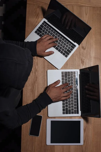 Vista aérea de hacker en sudadera con capucha negra usando computadoras portátiles, concepto de seguridad cibernética - foto de stock