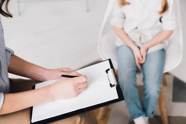 Plan recadré de psychologue avec presse-papiers vierges assis devant l'enfant — Photo de stock