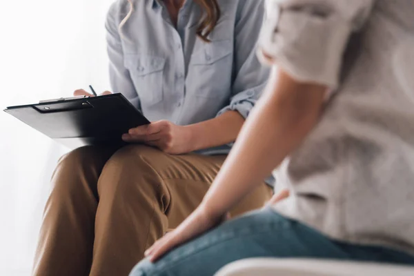 Cropped shot of psychologist with clipboard sitting in front of child — Stock Photo