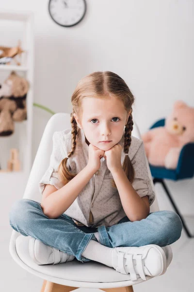Lonely little child sitting on chair and looking at camera — Stock Photo