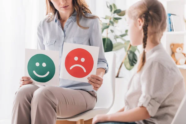 Cropped shot of psychologist showing happy and sad emotion faces cards to child — Stock Photo