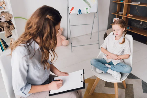 High angle view of psychologist with clipboard talking to little child in office — Stock Photo