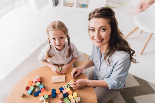 Vue grand angle de la mère heureuse et l'enfant regardant la caméra tout en jouant avec des blocs — Photo de stock