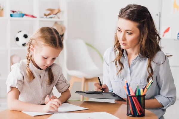 Psicólogo adulto sentado cerca de dibujo infantil con lápices de color - foto de stock