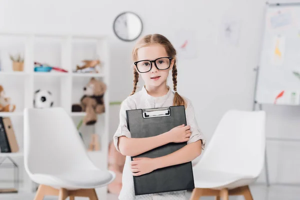 Petit enfant dans les lunettes tenant presse-papiers et regardant la caméra — Photo de stock