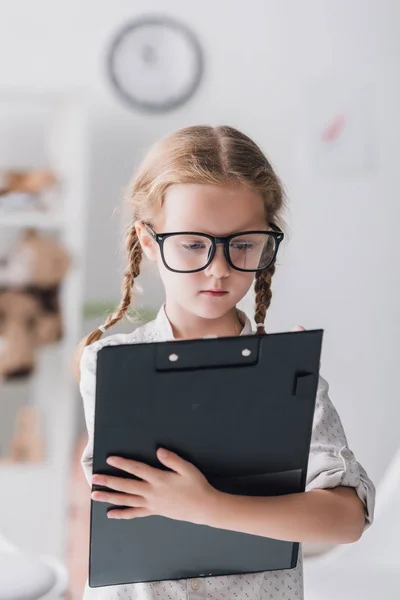 Nahaufnahme Porträt eines kleinen Kindes mit Brille, das im Klemmbrett schreibt — Stockfoto