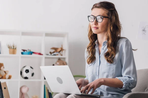 Close-up portrait of child psychologist sitting in armchair with laptop and looking away — Stock Photo