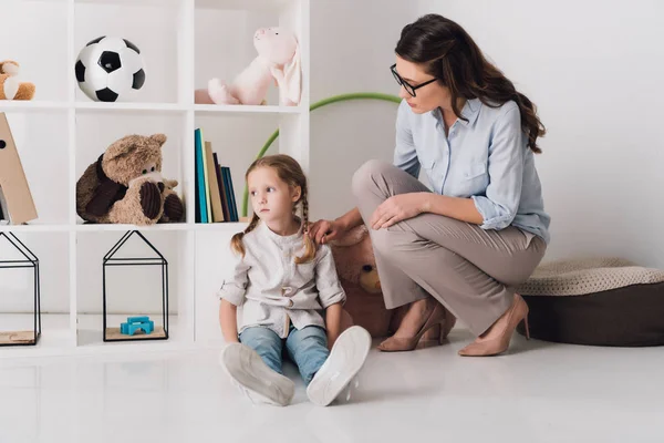 Psychologue féminine adulte soutenant enfant déprimé alors qu'elle est assise sur le sol — Photo de stock