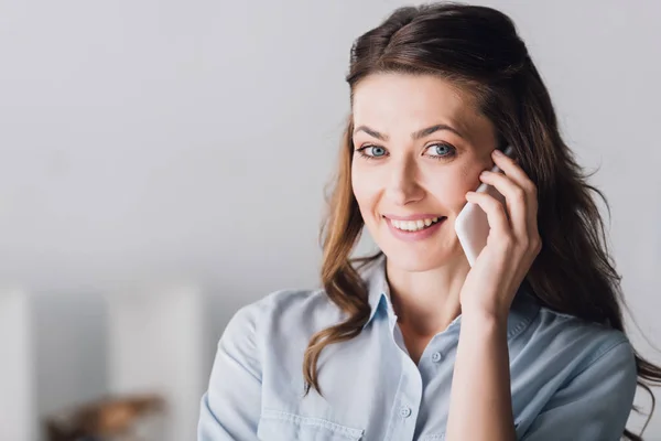 Close-up portrait of smiling adult woman talking by phone and looking at camera — Stock Photo