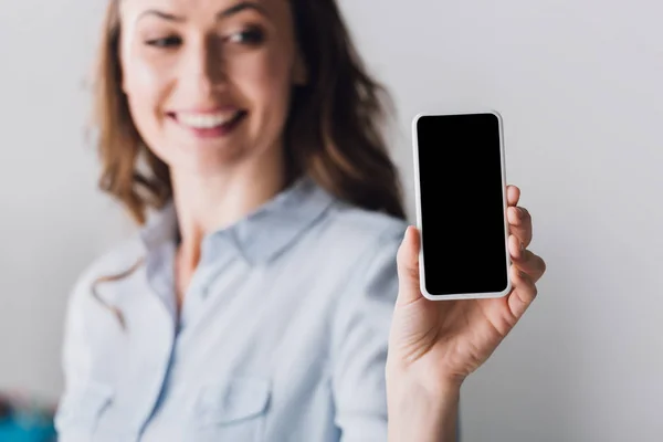 Close-up portrait of happy adult woman in shirt showing smartphone with blank screen at camera — Stock Photo