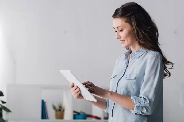 Smiling adult woman using tablet at home in front of shelves with toys — Stock Photo