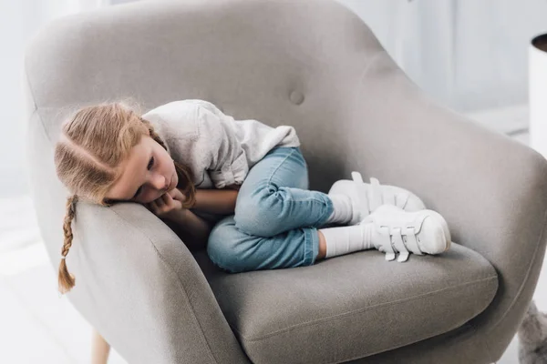 Triste niñito tumbado en sillón solo - foto de stock