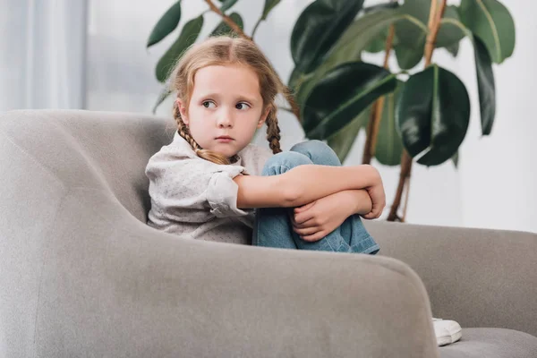 Lonely little child sitting in armchair and looking away — Stock Photo