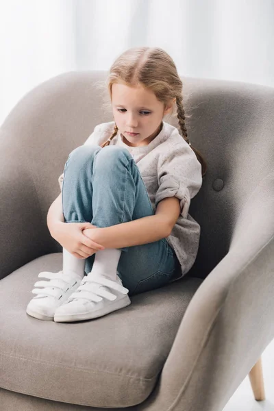 Lonely little child sitting in armchair and looking down — Stock Photo