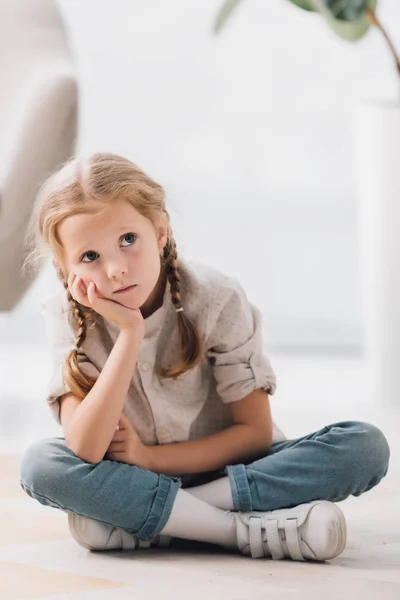 Criança pequena pensativa sentada no chão do quarto vazio e olhando para cima — Fotografia de Stock
