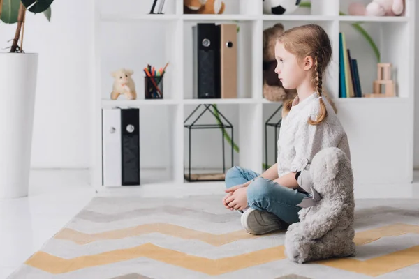 Side view of depressed little child sitting on floor with wooden blocks and looking away — Stock Photo